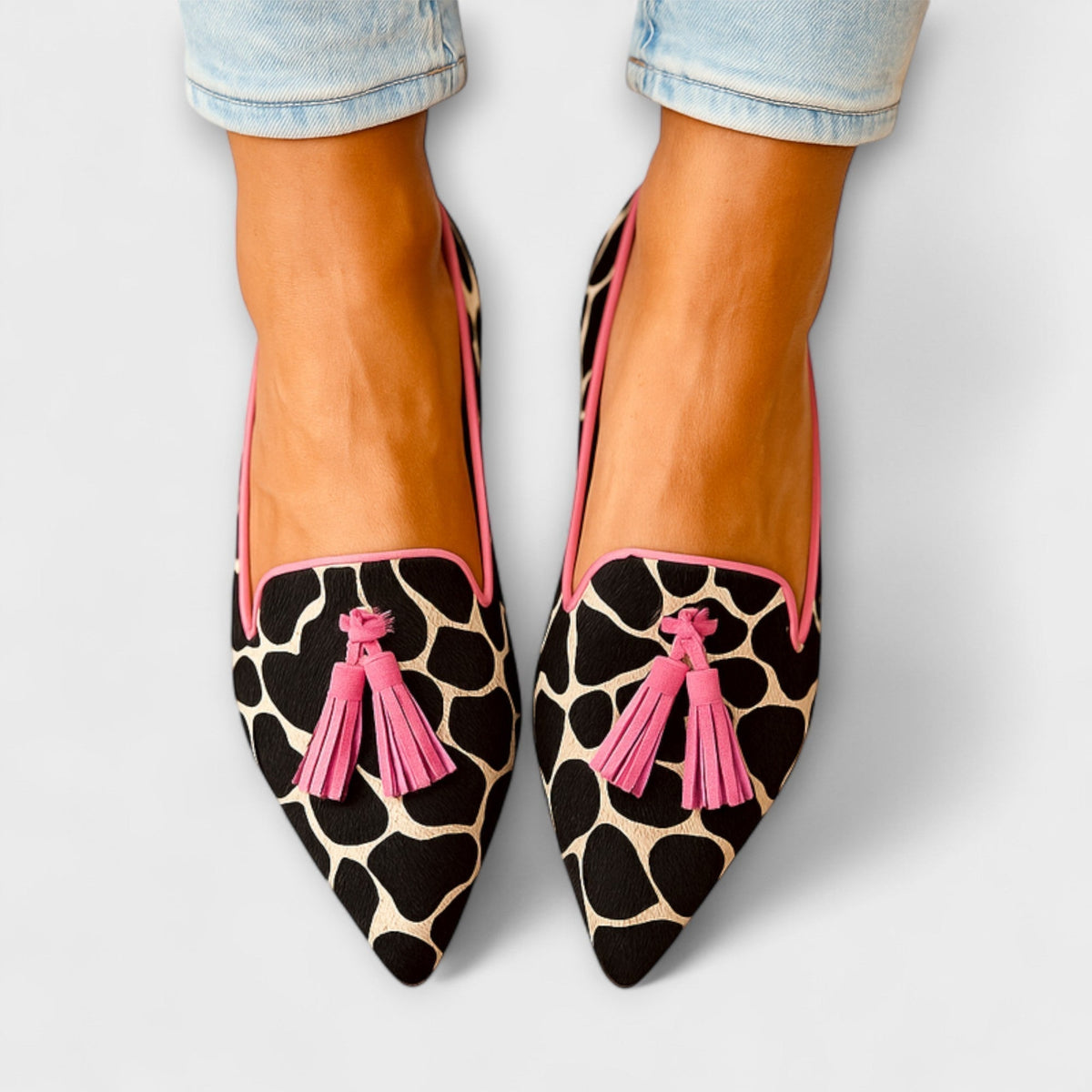 Lucia pointed loafers in black animal print with pink tassels, top view worn with jeans