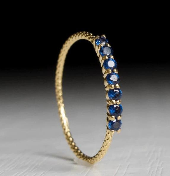 Seven-stone gold ring with deep blue-black stones, angled side view