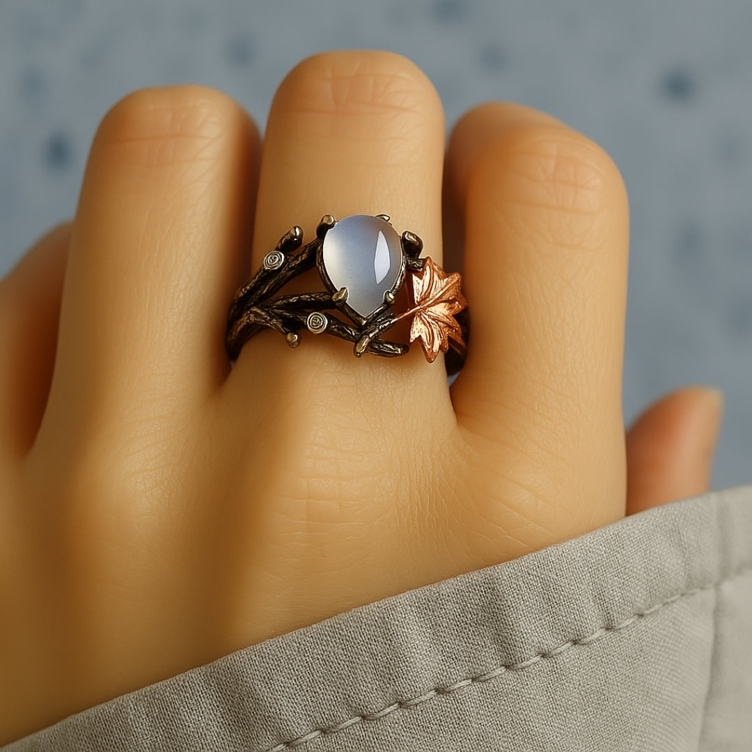 Moonstone ring worn on a hand, dark branch band with leaf detail