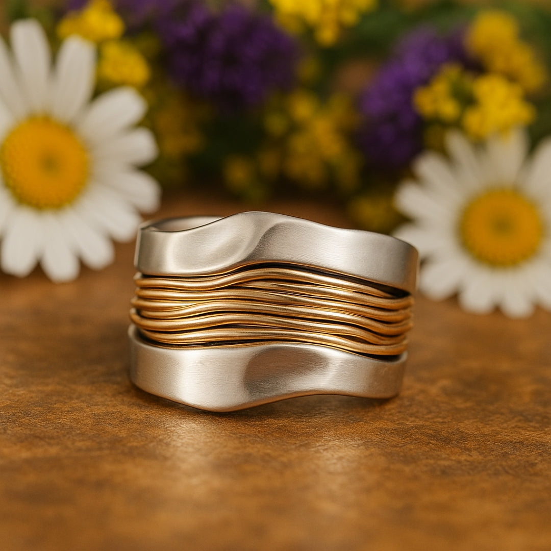 Silver and gold threads ring standing upright beside daisies
