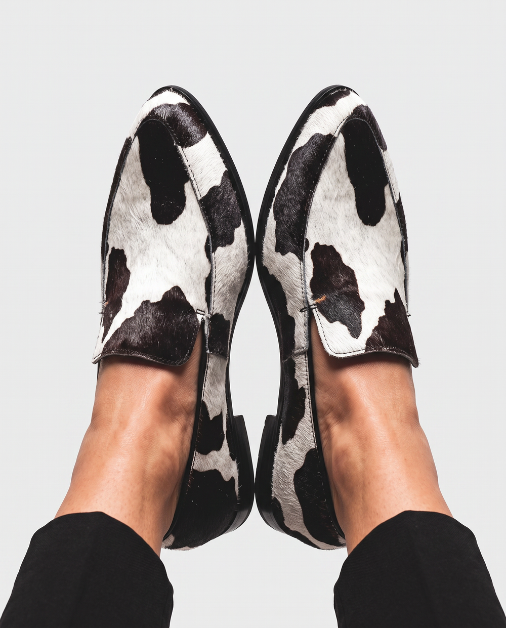 Bruna cow print loafers in black and white, overhead view on feet