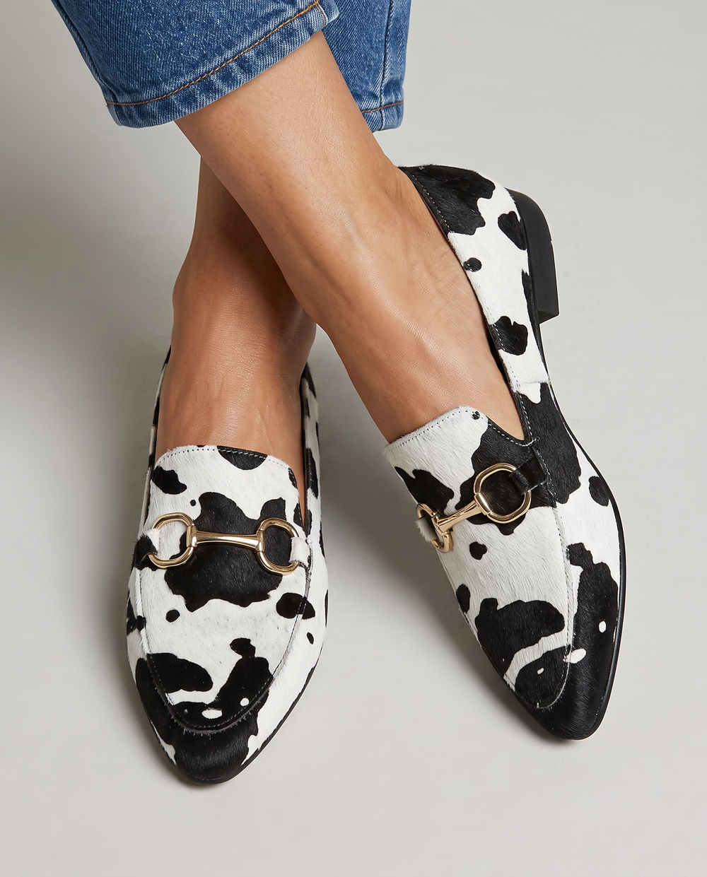 Black and white spotted hair-on loafers with gold bar detail, worn with jeans