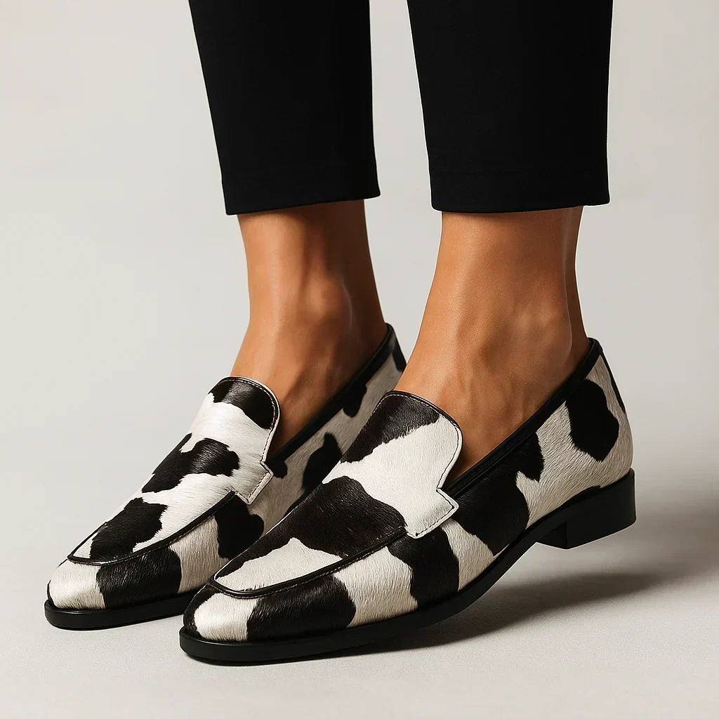 Josephine cow-print loafers worn with black trousers, front view