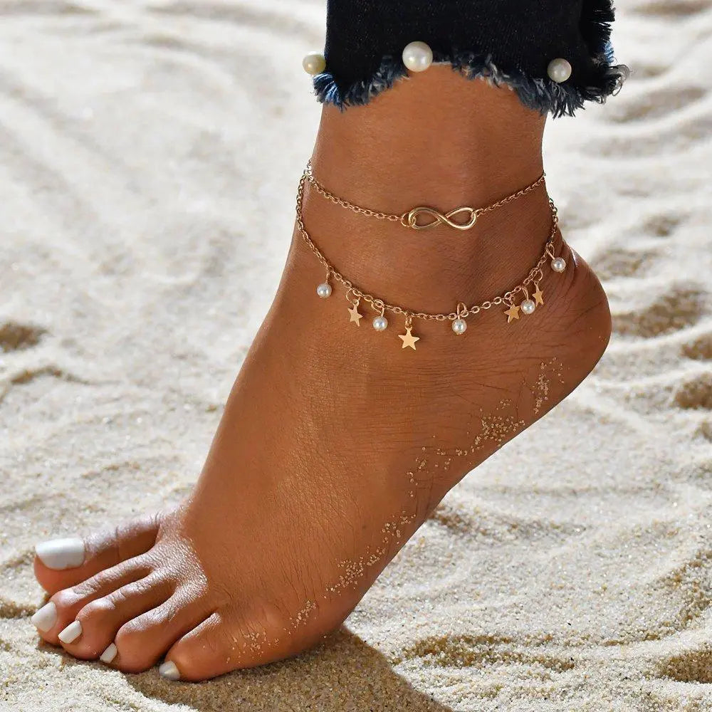 Infinity anklet with pearl and star charms in gold, worn on the ankle