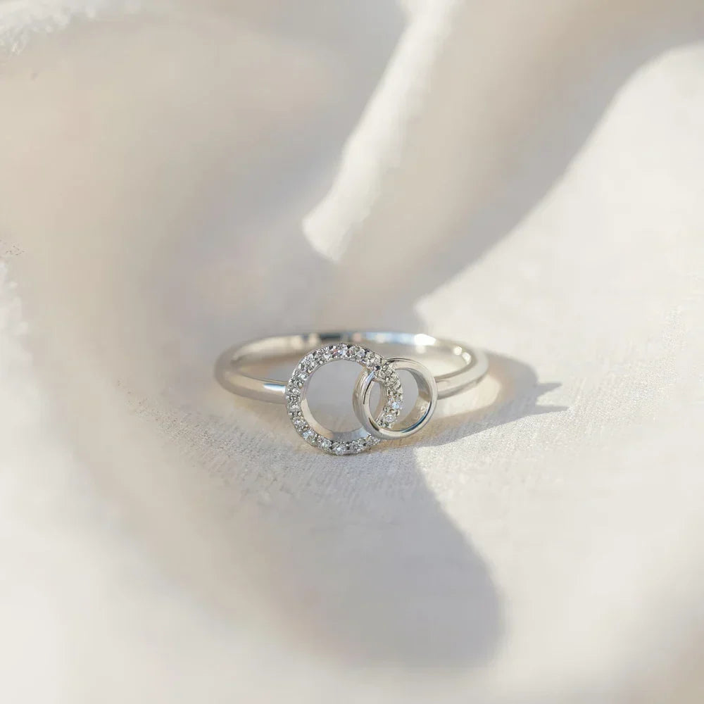 Sister ring in silver tone resting on soft fabric, angled view