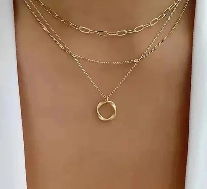 Layered gold chain necklace with round pendant worn at the neckline